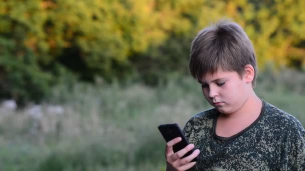 10 代の少年は、オープンエアでスマート フォンを使用してください。 — ストック動画