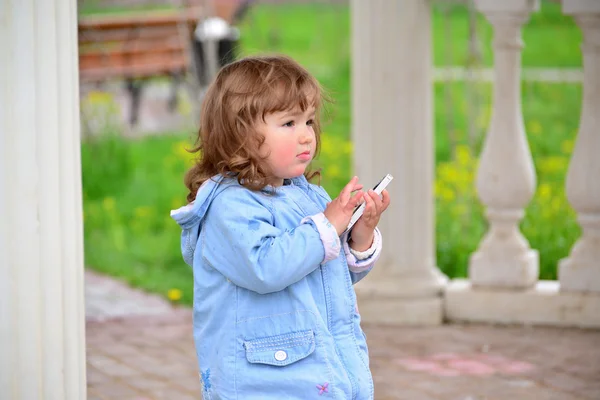 Flicka två år, med en mobiltelefon i parken — Stockfoto