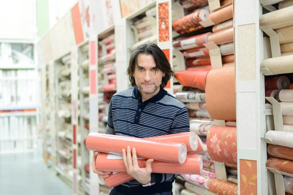 Hombre sosteniendo un rollo de papel pintado en la tienda — Foto de Stock