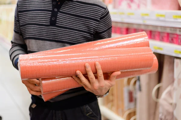 man holding a roll of wallpaper in the store