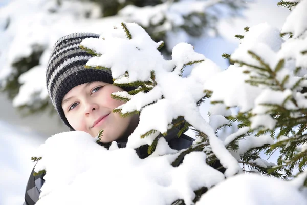 Adolescent garçon regarde hors de derrière arbres dans hiver forêt — Photo