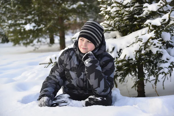 Teen pojke sitter på snö i vinter skogen — Stockfoto