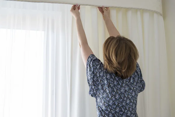 Wanita menggantung tirai putihnya di jendela — Stok Foto
