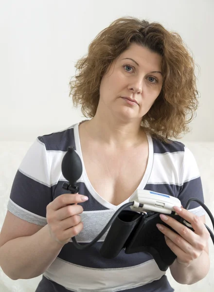 Взрослая женщина держит автоматический тонометр для измерения кровяного давления — стоковое фото