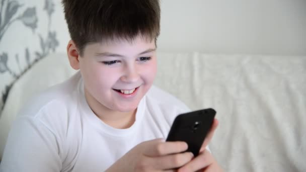 Мальчик играет на смартфоне и смеется — стоковое видео