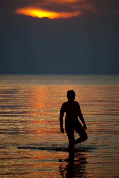 夕暮れ時の海の中の少年のシルエット — ストック写真