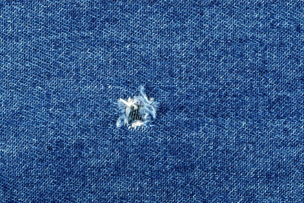 Hole on Denim Jeans. Ripped Destroyed Torn Blue jeans background. Close-up blue denim jeans texture
