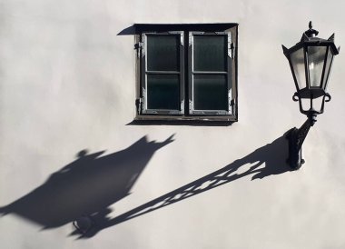 Eski model bir fener ve pencerenin yanındaki gölgesi güneşli bir günde eski bir evin temiz bir ışık duvarında.