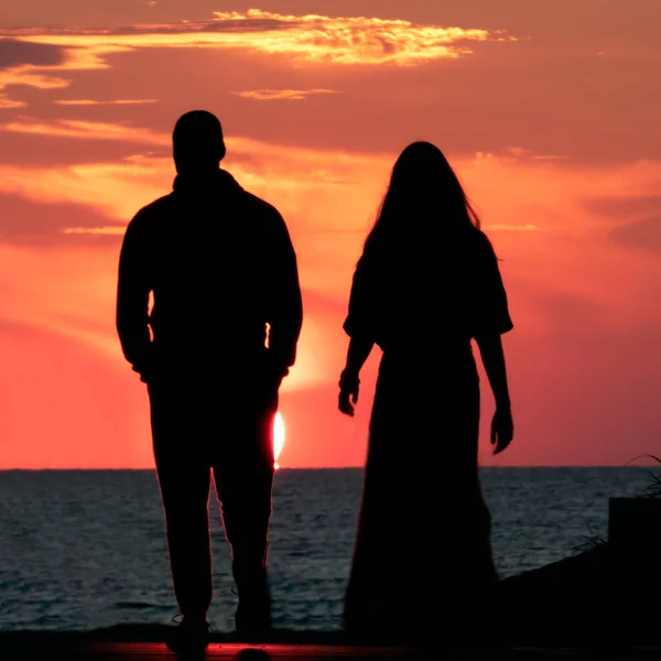 一对夫妇在日落背景下走向大海的轮廓 — 图库照片