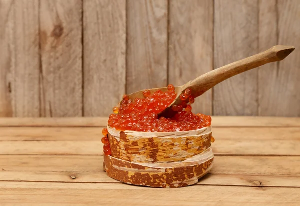 Red caviar on vintage background. Old wooden spoon and bowl made of bark. — Stock Photo, Image