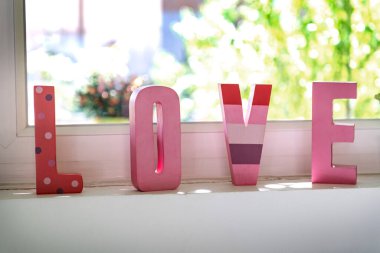 Arkasında bahçe olan pencerenin önünde 3 boyutlu pembe harfler. Aşk ve Sevgililer Günü. Evdeki mutluluk.