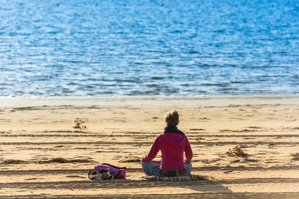 女孩坐在水边的沙滩上 — 图库照片