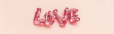 Sevgililer Günü yaratıcı konsepti. Şişirilebilir pembe folyomsu balon pembe arka planda aşk kelimesini şekillendirdi. Üst görünüm düzlüğü kopyalama alanı ile yatıyordu. Tatil, kutlama, bekarlığa veda partisi dekorasyonu.