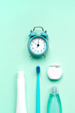 Diş hijyeni, ağız bakımı ürünleri ve yeşil naneli arkaplan üzerindeki alarm saati fotokopi alanı ile. Boş diş macunu tüpü, diş ipi ve diş fırçası. Düz konum, üst görünüm bileşimi, model