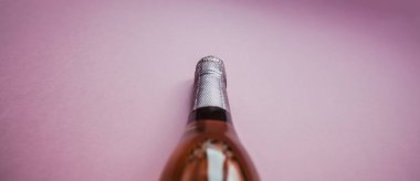 Pembe arka planda minimum kompozisyonda bir şişe gül şampanyası ve fotokopi alanı. Doğal ışık. Tatma şablonu, degustation davetiye kartı. Yan görünüm