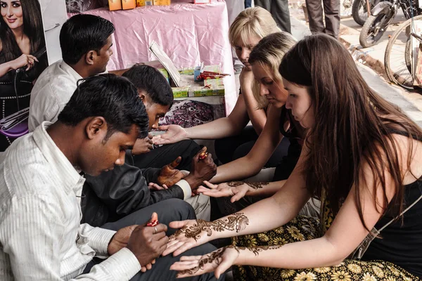 Varanasi, Indien - November 13, 2012: indian street master använder henna klistra eller mehndi tillämpning å vit turist kvinna. Traditionella indiska naturliga hud dekoration, bio-tatuering — Stockfoto