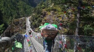 Khumbu 'da askı köprüsünde yürüyen hamallar ve turistler. Himalaya, Nepal