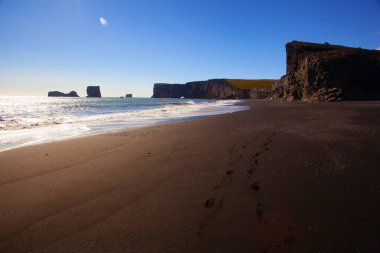 İzlanda 'daki siyah kum Reynisfjara Sahili. Gün batımında okyanus sahilindeki kayalıklar ve kayalıklar. İzlanda 'nın güney kıyısında popüler bir turizm merkezi..