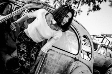 Güzel genç kız eski arabanın yanında poz veriyor.