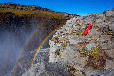 Detifoss şelalesinin yanındaki kırmızı elbiseli kadın çift gökkuşağı, İzlanda