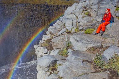 Detifoss şelalesinin yanındaki kırmızı elbiseli kadın çift gökkuşağı, İzlanda