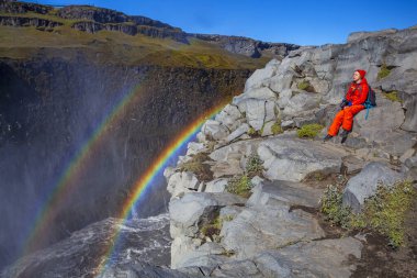 Detifoss şelalesinin yanındaki kırmızı elbiseli kadın çift gökkuşağı, İzlanda