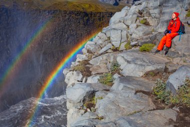 Detifoss şelalesinin yanındaki kırmızı elbiseli kadın çift gökkuşağı, İzlanda