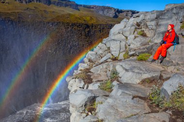 Detifoss şelalesinin yanındaki kırmızı elbiseli kadın çift gökkuşağı, İzlanda