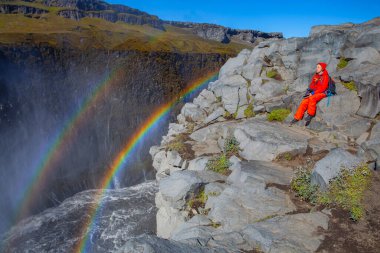Detifoss şelalesinin yanındaki kırmızı elbiseli kadın çift gökkuşağı, İzlanda