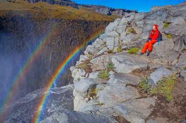 Detifoss şelalesinin yanındaki kırmızı elbiseli kadın çift gökkuşağı, İzlanda
