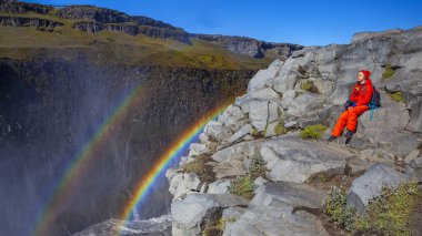 Detifoss şelalesinin yanındaki kırmızı elbiseli kadın çift gökkuşağı, İzlanda