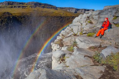 Detifoss şelalesinin yanındaki kırmızı elbiseli kadın çift gökkuşağı, İzlanda