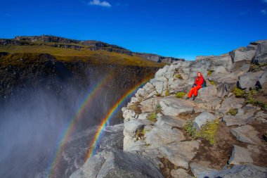 Detifoss şelalesinin yanındaki kırmızı elbiseli kadın çift gökkuşağı, İzlanda
