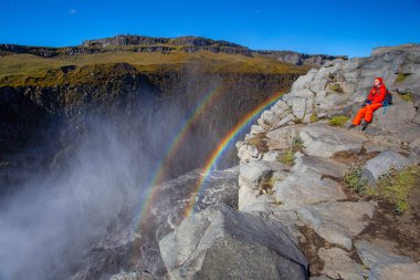 Detifoss şelalesinin yanındaki kırmızı elbiseli kadın çift gökkuşağı, İzlanda