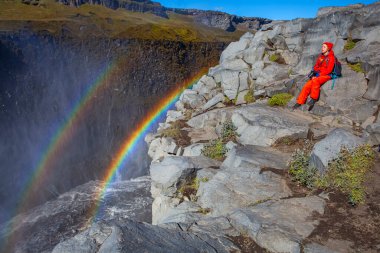 Detifoss şelalesinin yanındaki kırmızı elbiseli kadın çift gökkuşağı, İzlanda