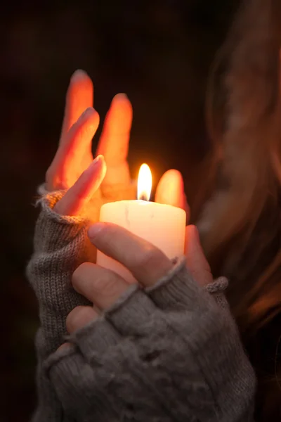 Jeune femme regardant une bougie mains priantes avec une bougie en arrière-plan sombre — Photo