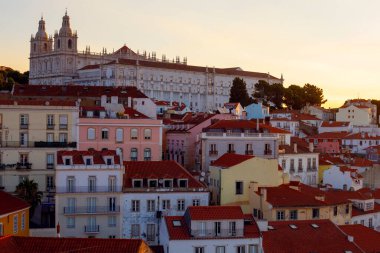 Lizbon, Portekiz - 27 Temmuz 2025: Lizbon 'un ikonik kırmızı kiremitli çatılarının çarpıcı bir panoramik gün doğumu görüntüsü, gündoğumu sırasındaki tarihi mimari