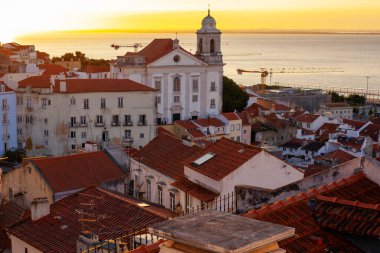 Lizbon, Portekiz - 27 Temmuz 2025: Lizbon 'un ikonik kırmızı kiremitli çatılarının çarpıcı bir panoramik gün doğumu görüntüsü, gündoğumu sırasındaki tarihi mimari