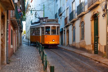Lizbon, Portekiz - 27 Temmuz 2025: Klasik bir ünlü sarı tramvay Lizbon 'daki canlı kırmızı tarihi binalardan sabah erken saatlerde geçiyor