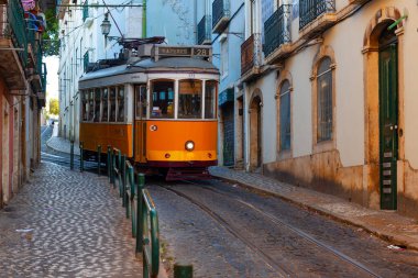 Lizbon, Portekiz - 27 Temmuz 2025: Klasik bir ünlü sarı tramvay Lizbon 'daki canlı kırmızı tarihi binalardan sabah erken saatlerde geçiyor