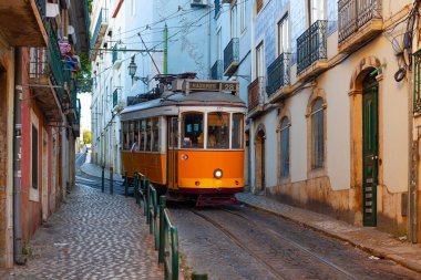 Lizbon, Portekiz - 27 Temmuz 2025: Klasik bir ünlü sarı tramvay Lizbon 'daki canlı kırmızı tarihi binalardan sabah erken saatlerde geçiyor
