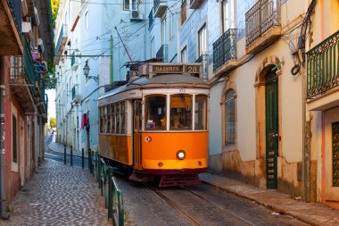 Lizbon, Portekiz - 27 Temmuz 2025: Klasik bir ünlü sarı tramvay Lizbon 'daki canlı kırmızı tarihi binalardan sabah erken saatlerde geçiyor