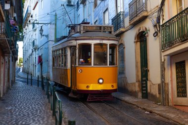 Lizbon, Portekiz - 27 Temmuz 2025: Klasik bir ünlü sarı tramvay Lizbon 'daki canlı kırmızı tarihi binalardan sabah erken saatlerde geçiyor