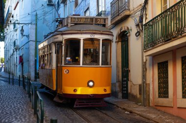 Lizbon, Portekiz - 27 Temmuz 2025: Klasik bir ünlü sarı tramvay Lizbon 'daki canlı kırmızı tarihi binalardan sabah erken saatlerde geçiyor