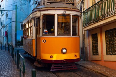 Lizbon, Portekiz - 27 Temmuz 2025: Klasik bir ünlü sarı tramvay Lizbon 'daki canlı kırmızı tarihi binalardan sabah erken saatlerde geçiyor