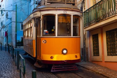 Lizbon, Portekiz - 27 Temmuz 2025: Klasik bir ünlü sarı tramvay Lizbon 'daki canlı kırmızı tarihi binalardan sabah erken saatlerde geçiyor