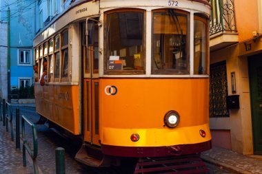 Lizbon, Portekiz - 27 Temmuz 2025: Klasik bir ünlü sarı tramvay Lizbon 'daki canlı kırmızı tarihi binalardan sabah erken saatlerde geçiyor