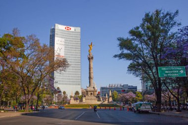 Mexico City, Meksika - 14 Mart 2022: Güneşli bir bahar gününde Özgürlük Anıtı ve döner kavşak, modern binalar ve arka planda çiçek açan Jacaranda ağaçları
