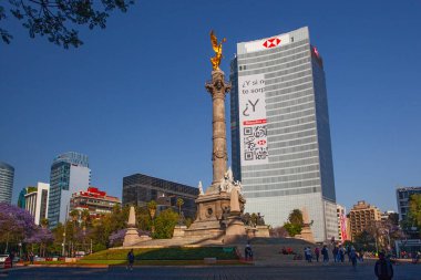 Mexico City, Meksika - 14 Mart 2022: Güneşli bir bahar gününde Özgürlük Anıtı ve döner kavşak, modern binalar ve arka planda çiçek açan Jacaranda ağaçları