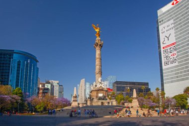 Mexico City, Meksika - 14 Mart 2022: Güneşli bir bahar gününde Özgürlük Anıtı ve döner kavşak, modern binalar ve arka planda çiçek açan Jacaranda ağaçları
